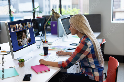 Caucasian woman in office having video call with diverse colleagues displayed on computer screen