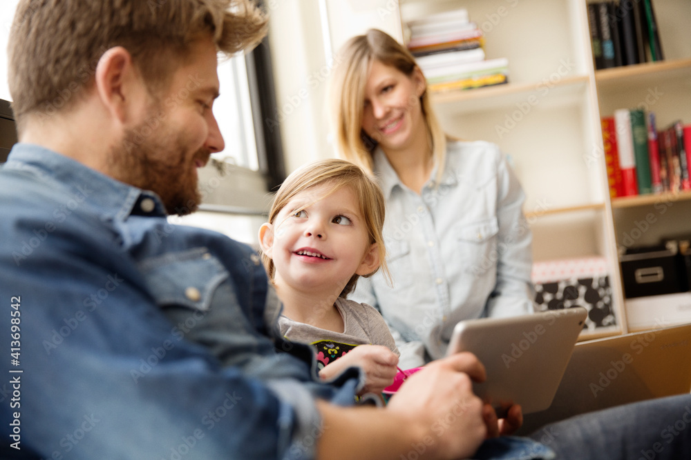 Girl looking at father holding digital tablet with woman in background Girl looking at father holding digital tablet with woman in background