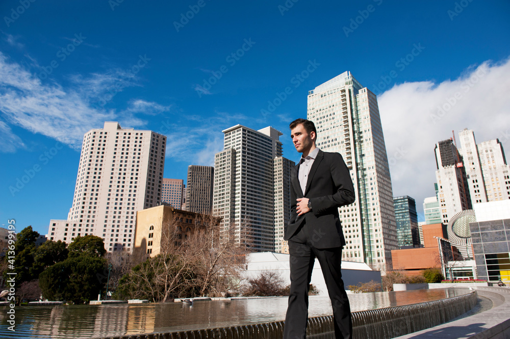 Low angle view of businessman walking by pond against buildings on sunny day Low angle view of businessman walking by pond against buildings on sunny day