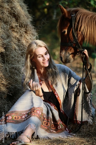 A girl in a blanket with a horse at a haystack