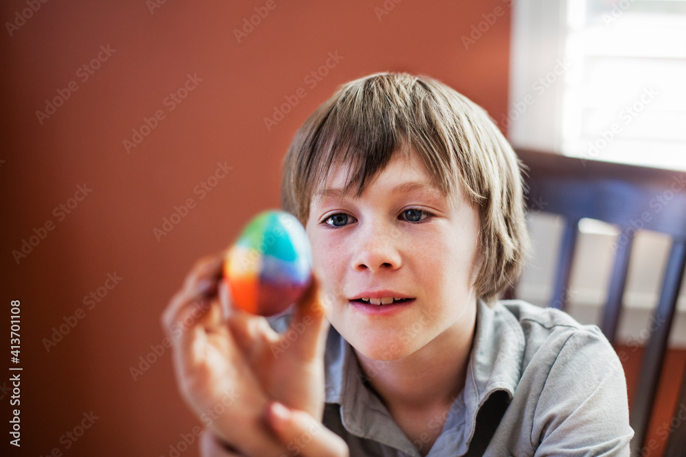 Boy looking at decorated Easter egg while sitting on chair at home Boy looking at decorated Easter egg while sitting on chair at home