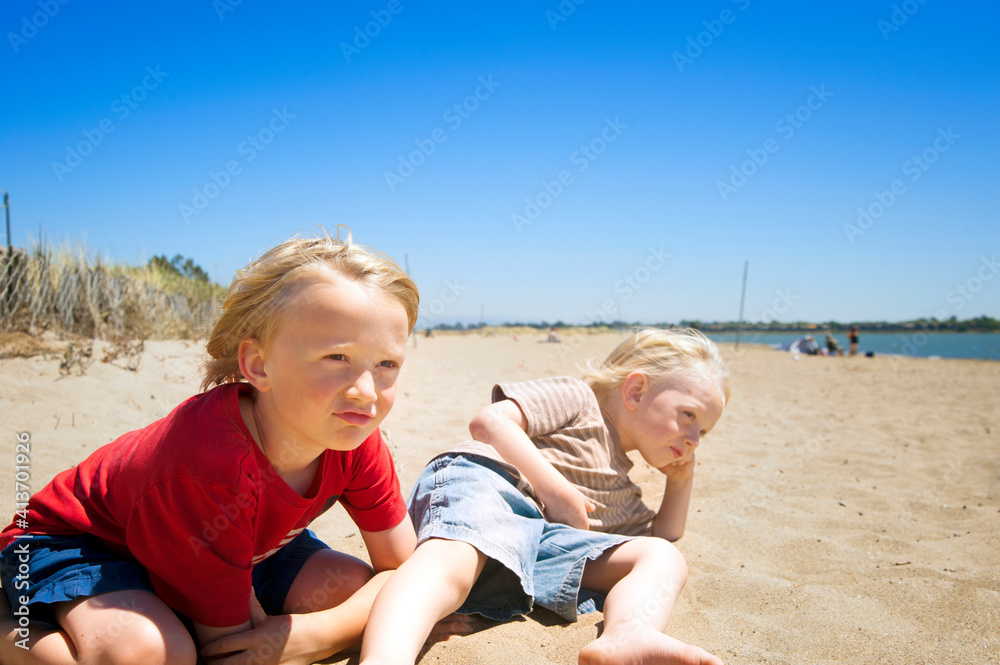 Siblings relaxing at beach against clear sky Siblings relaxing at beach against clear sky