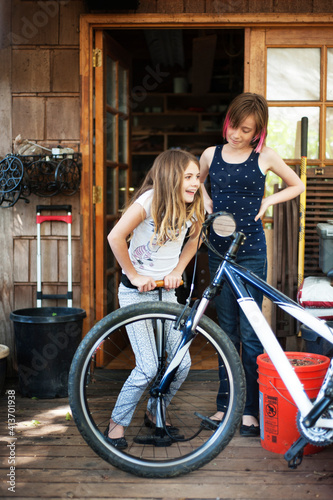 Girl looking at sister inflating bicycle tire while standing on porch photo