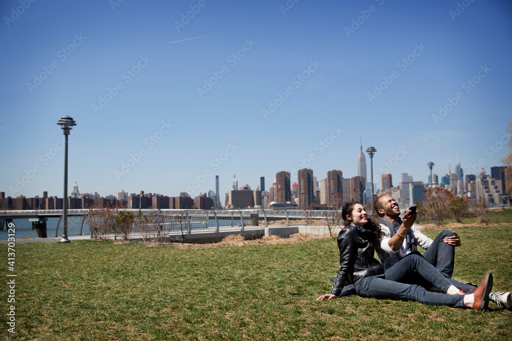 Cheerful couple using mobile phone while relaxing on field against blue sky Cheerful couple using mobile phone while relaxing on field against blue sky