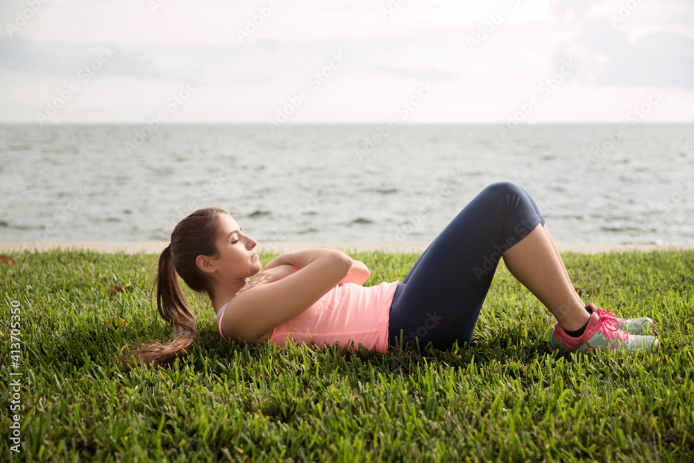 Side view of woman exercising on grassy field against sea Side view of woman exercising on grassy field against sea