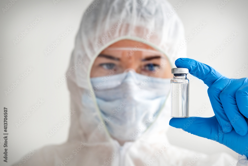 Doctor holds in protective medical suit vial with vaccine in his hands. COVID-19 vaccination concept Doctor holds in protective medical suit vial with vaccine in his hands. COVID-19 vaccination concept