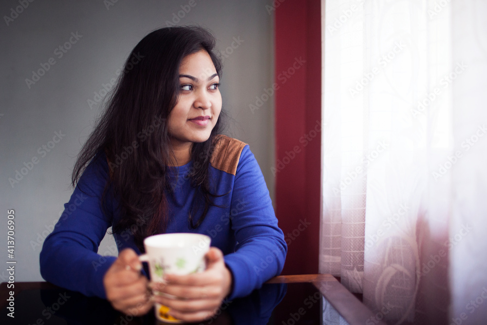 © Cavan Images - Smiling thoughtful woman holding coffee cup while sitting at table
