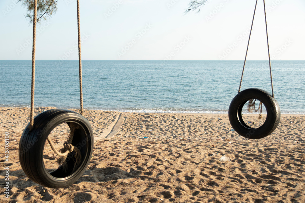 Tire swings hang from trees on the sandy beach. With a background of blue sea and sky with coluds