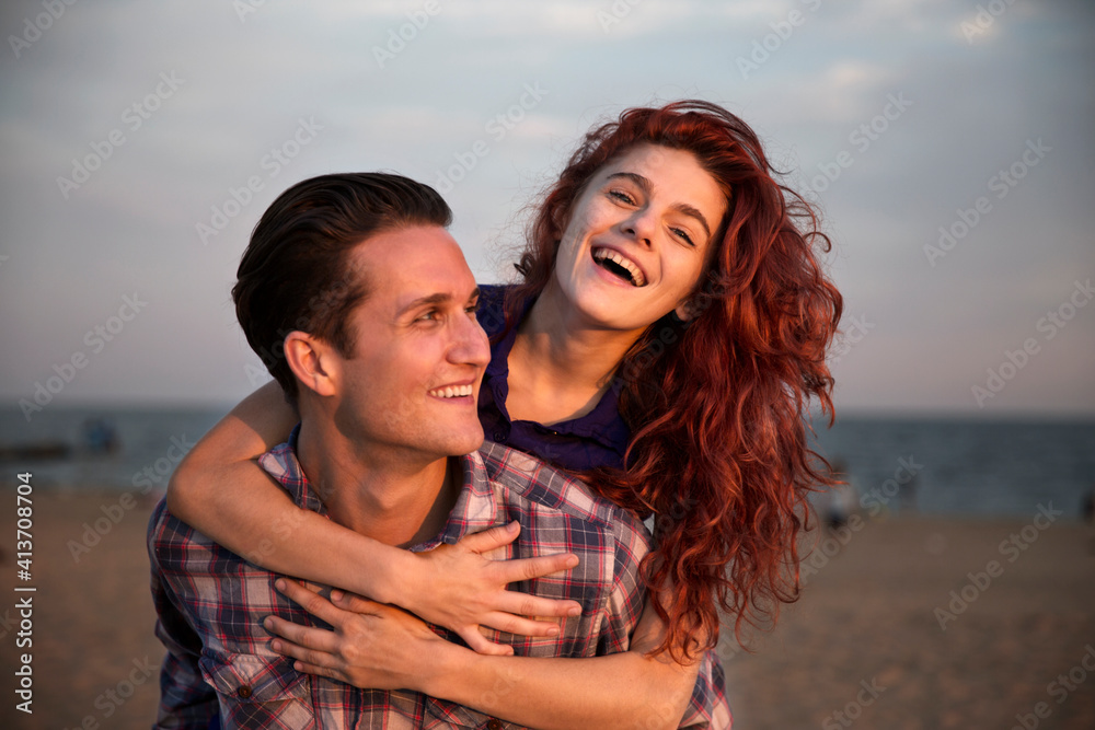 Happy man piggybacking woman at beach during sunset