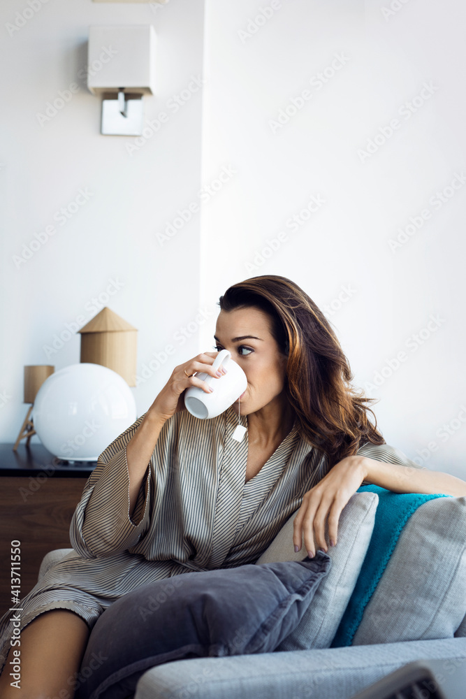 Woman drinking tea while relaxing on armchair at home Woman drinking tea while relaxing on armchair at home