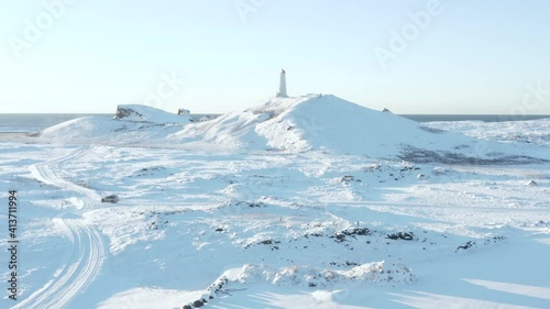 White winter landscape at Reykjanes Lighthouse on hill and car driving on road photo