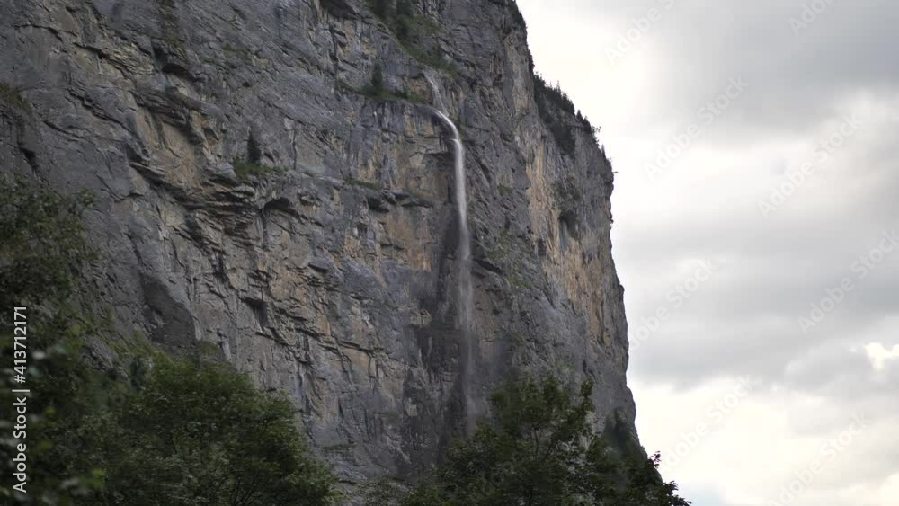 Water falling down between the rocks and green pine trees from a high waterfall in Lauterbrunnen in Switserland on a cloudy day. Wide shot Water falling down between the rocks and green pine trees from a high waterfall in Lauterbrunnen in Switserland on a cloudy day. Wide shot