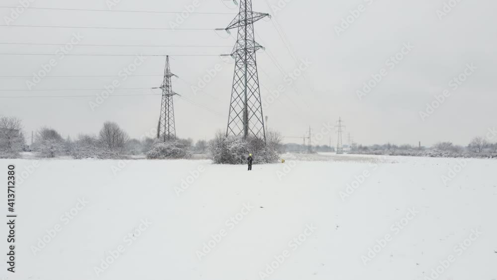 Technician checking High Voltage power line wires with tablet and yellow helmet during a snow storm. Breakdown failure due ice frozen low temperature, city blackout isolation