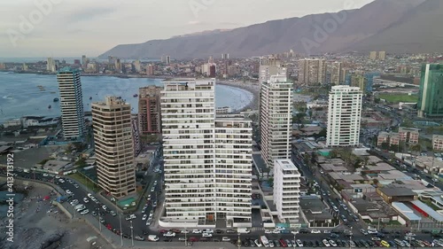 Sideways drone flight past tall buildings near the sea and in the background you can see a city with cars with high mountains. photo
