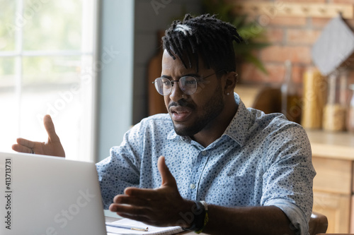 Close up angry annoyed African American man wearing glasses having problem with broken laptop, computer crash, data loss, looking at screen, unhappy confused businessman reading unexpected bad news