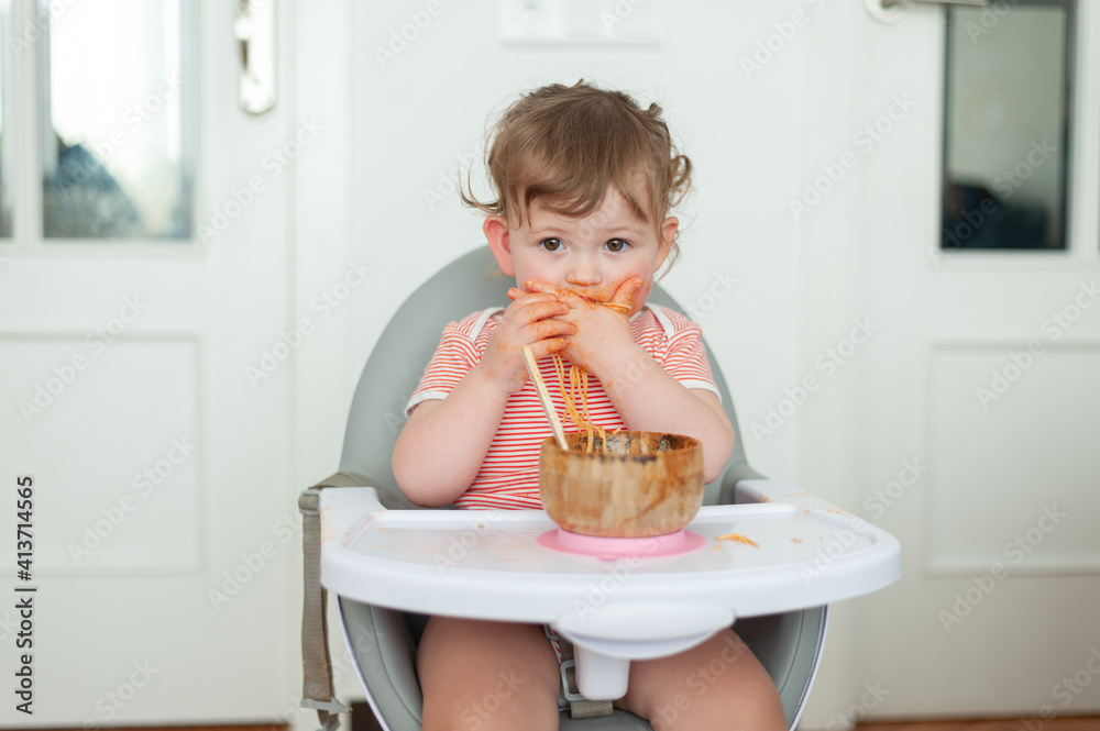 Baby girl eating pasta for lunch sitting in high chair Baby girl eating pasta for lunch sitting in high chair