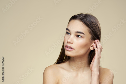 Woman with bared shoulders dark hair clean skin makeup beige background