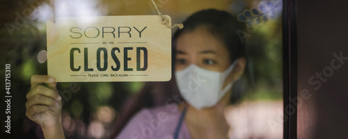 Close up shot of woman wearing mask and hand turning closed sign board on glass door in coffee shop and restaurant after covid-19 lockdown quarantine.Business crisis concept.