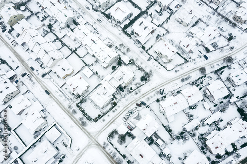 flying above snow-covered houses and streets in suburban neighborhood on a winter cold day