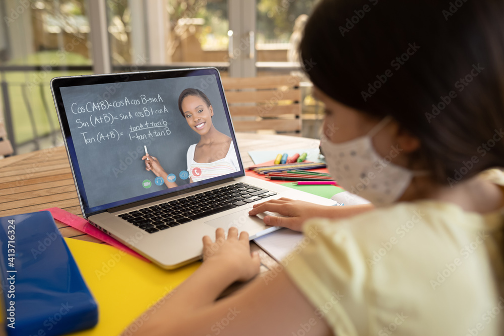 Female student wearing face mask having a video call with female teacher on laptop at school Female student wearing face mask having a video call with female teacher on laptop at school