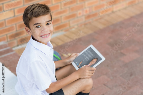 Portrait of male caucasian student having a video call with female teacher on digital tablet at scho photo