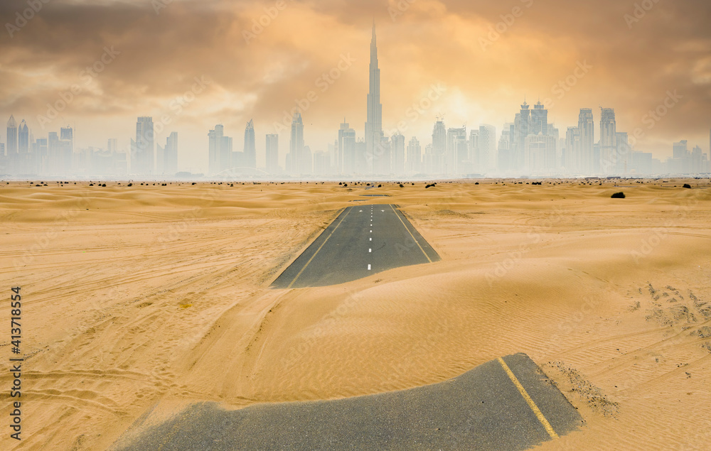 View from above, stunning aerial view of a deserted road covered by sand dunes with the Dubai Skyline in the background. Dubai, United Arab Emirates.