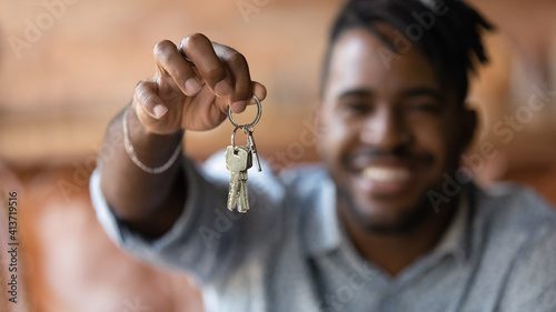 Close up blurred background satisfied African American man customer showing keys at camera, purchase first own apartment, young tenant excited by relocation, mortgage and real estate concept photo