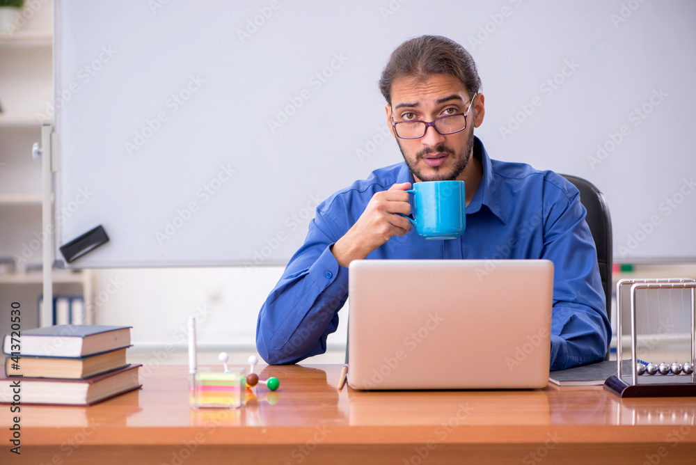 Young male teacher physicist sitting in the classroom