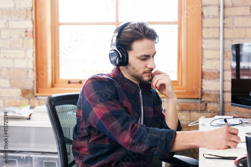 Businessman wearing headphones writing on diary while working in office photo