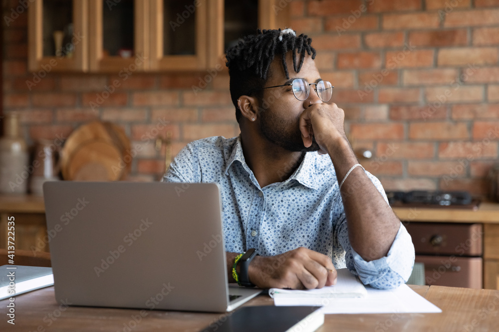 Close up thoughtful African American man wearing glasses pondering strategy, sitting at table with laptop, looking to aside, touching chin, pensive businessman or student working on research project - obrazy, fototapety, plakaty 