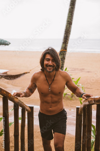 Portrait of shirtless man standing by wooden railing at beach photo