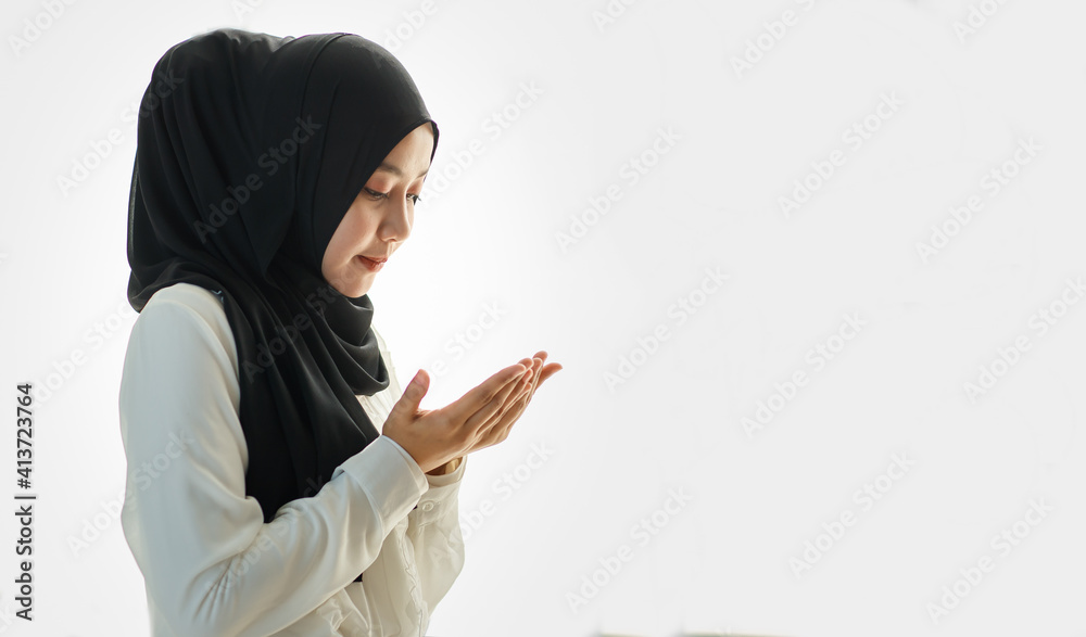 Young and beautiful Asian Muslim woman in black veil sitting on floor and praying with respect and calm manner Young and beautiful Asian Muslim woman in black veil sitting on floor and praying with respect and calm manner