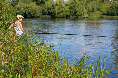 A girl with a fishing rod in her hands is fishing on the river.