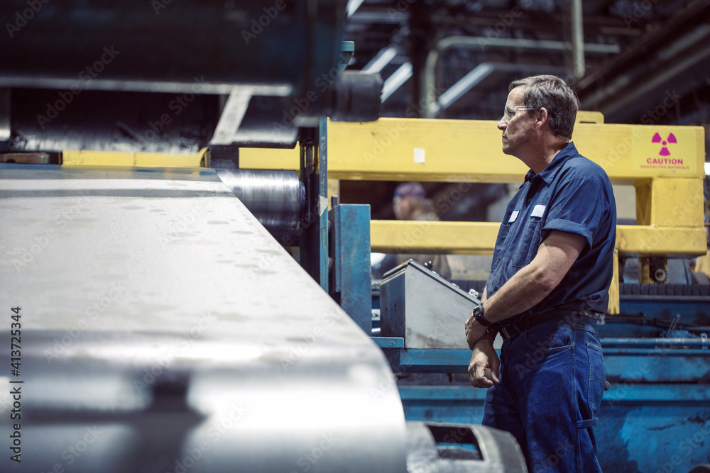Manual worker looking at machine manufacturing sheet steel in factory Manual worker looking at machine manufacturing sheet steel in factory