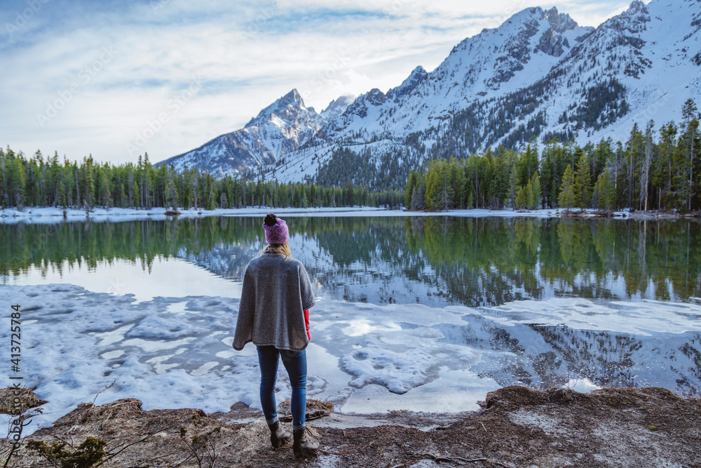Rear view of woman standing by lake against mountains during winter Rear view of woman standing by lake against mountains during winter