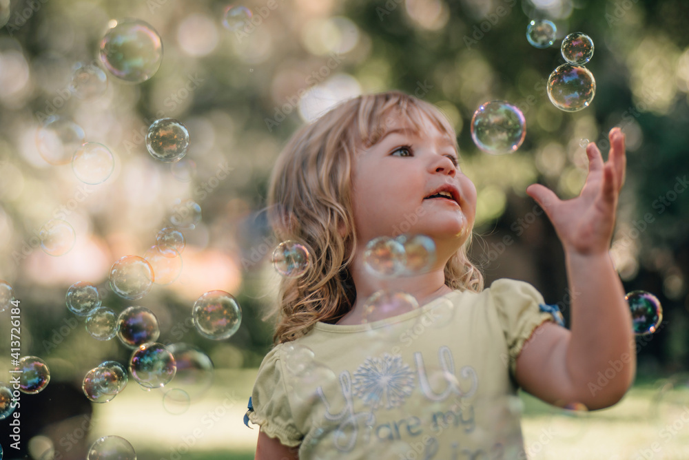 Cute baby girl reaching for bubbles flying in air at park Cute baby girl reaching for bubbles flying in air at park