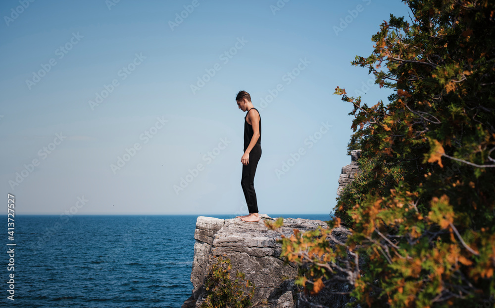 Full length of hiker standing on cliff against sea and clear sky at Bruce Peninsula National Park Full length of hiker standing on cliff against sea and clear sky at Bruce Peninsula National Park