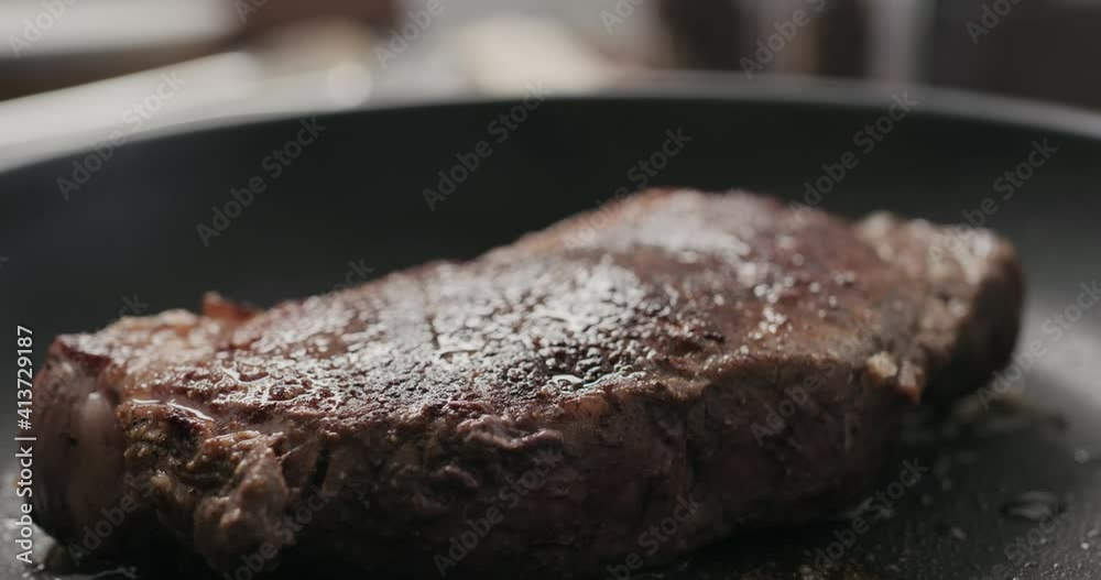 Slow motion handheld shot of new york steak on nonstick pan Slow motion handheld shot of new york steak on nonstick pan