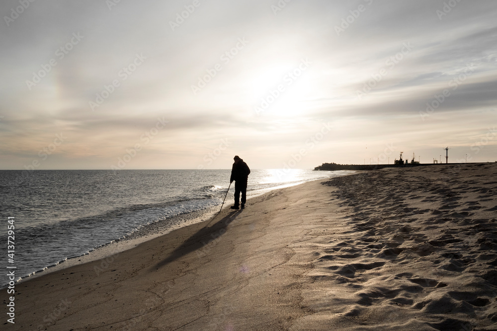 Szerokie ujęcie pod światło samotnego mężczyzny spacerującego brzegiem morza - obrazy, fototapety, plakaty 