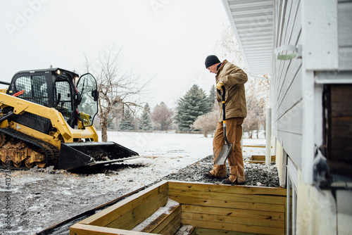 Side view of man holding shovel working in backyard against sky during winter