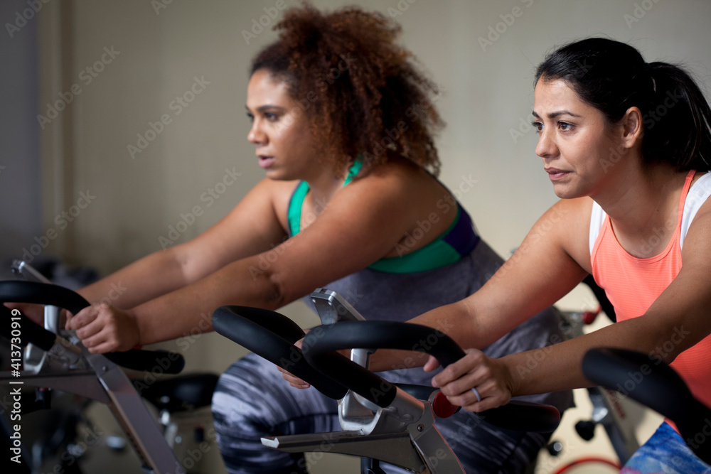 Female friends exercising on exercise bikes in gym