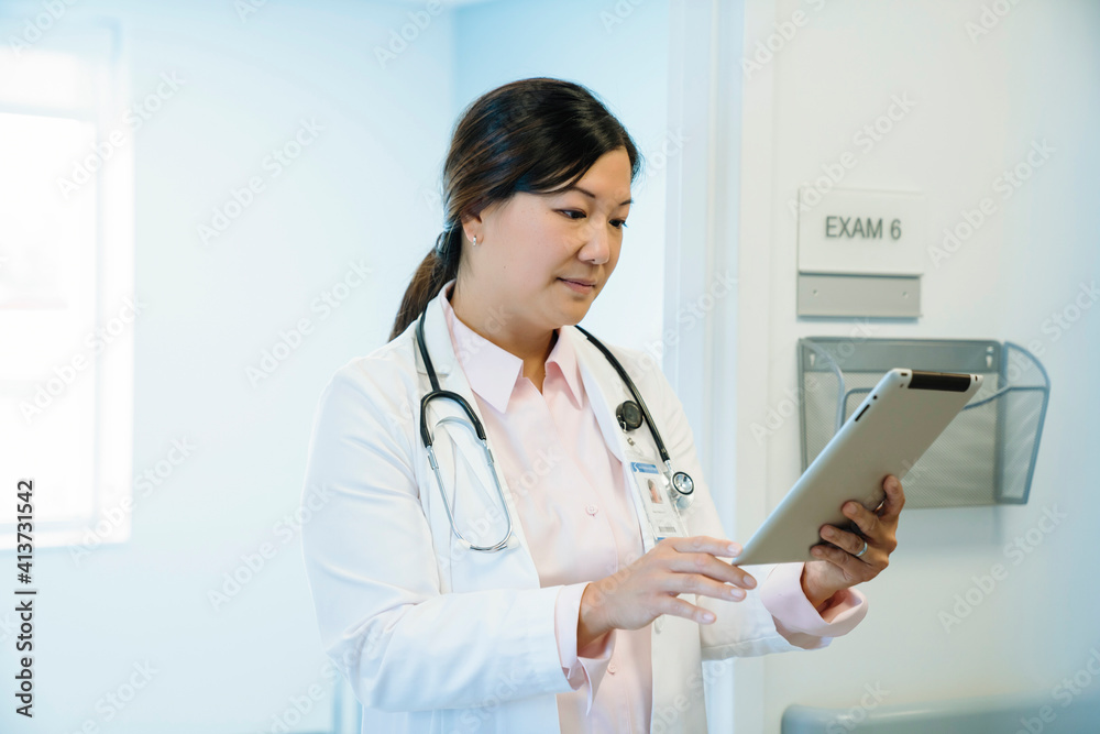 Female doctor looking at tablet computer while standing in hospital corridor Female doctor looking at tablet computer while standing in hospital corridor