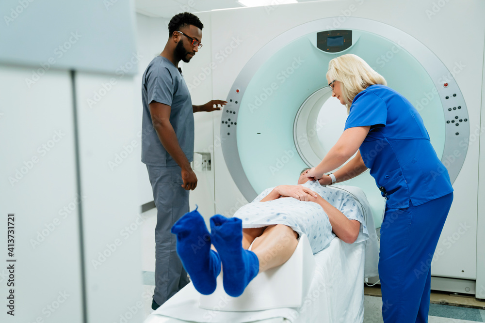 Doctor looking at nurse preparing for MRI Scan on patient in examination room Doctor looking at nurse preparing for MRI Scan on patient in examination room