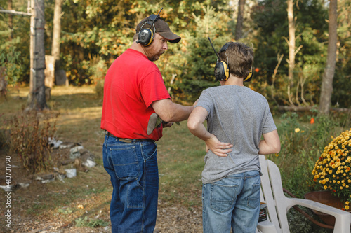 Father teaching son to shoot weapon at backyard photo