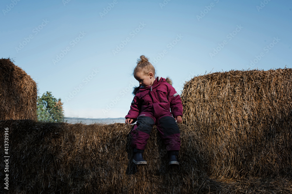 Full length of girl sitting on hay bale against clear sky Full length of girl sitting on hay bale against clear sky