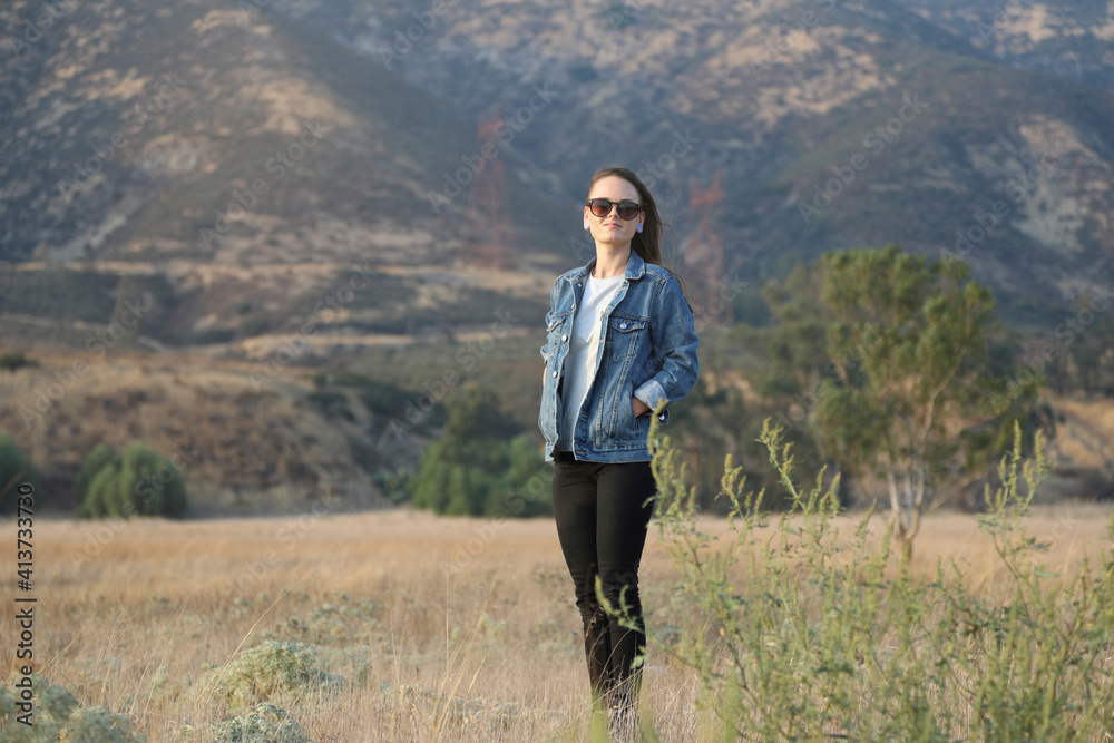 Confident young woman with hands in pockets standing against mountain on field Confident young woman with hands in pockets standing against mountain on field