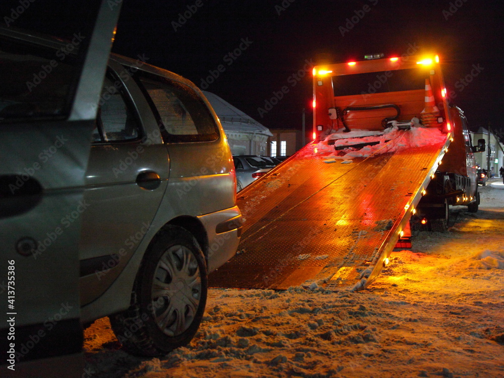 Loading a car on a tow truck lighted platform close up side view on a winter night on the snow covered Parking, technical assistance to the driver