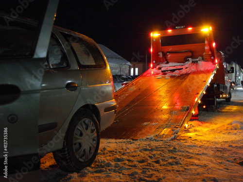 Loading a car on a tow truck lighted platform close up side view on a winter night on the snow covered Parking, technical assistance to the driver photo