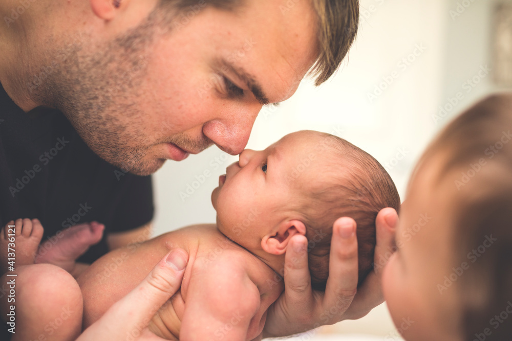 Father carrying newborn daughter while sitting by son at home Father carrying newborn daughter while sitting by son at home