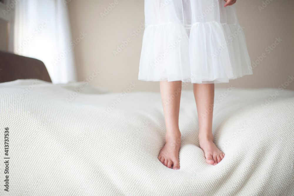 Low section of girl standing on bed at home